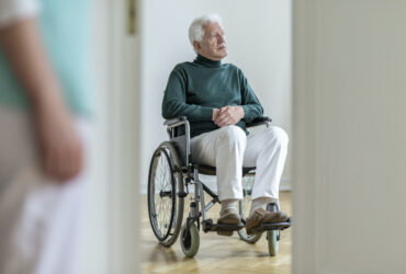 Sad disabled elderly man in a wheelchair in the hospital. Blurre
